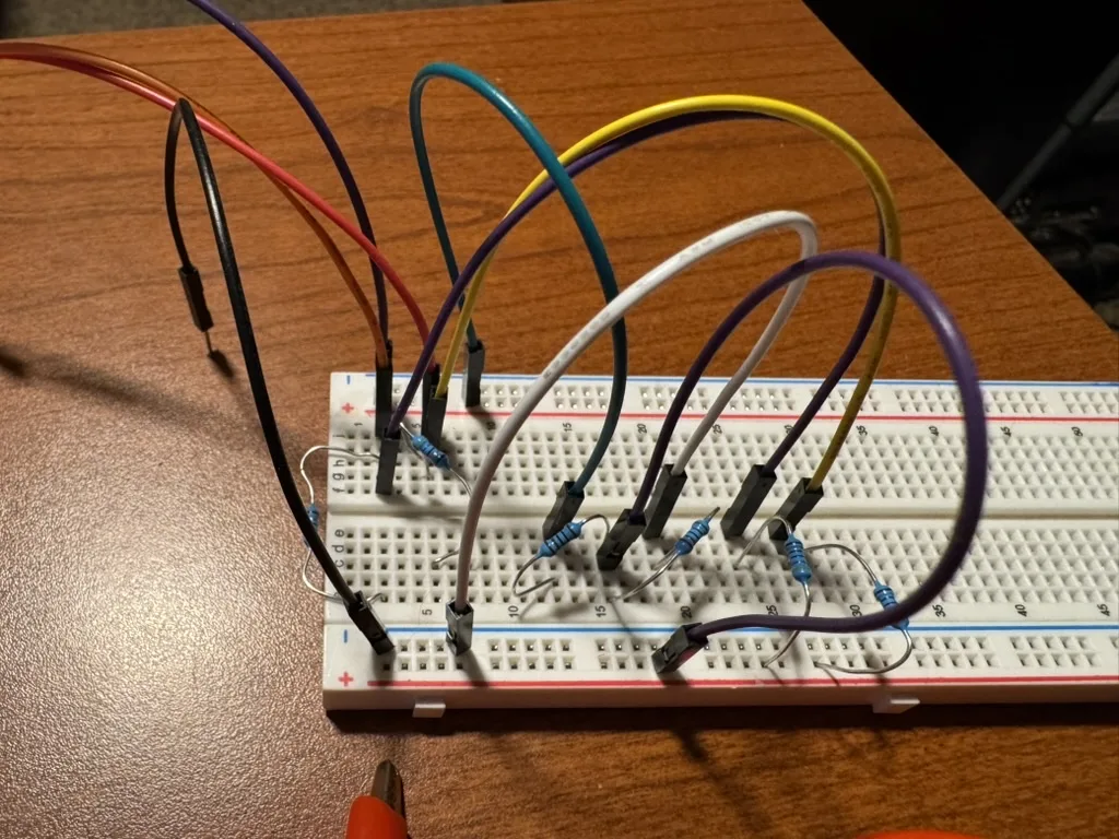 A breadboard with a row of pull-up resistors and coloured jumper wires arcing off to a controller cable