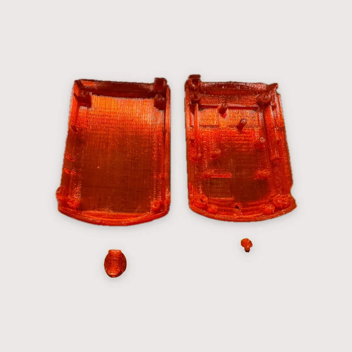 The two halves of a translucent red printed VMU shell laid open side by side, with two small printed parts below them